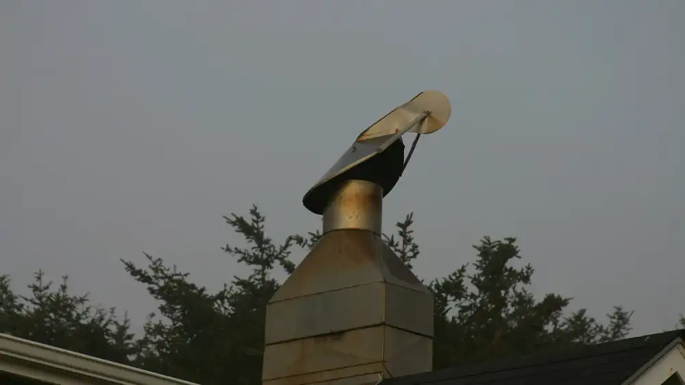 A mesh-sided chimney cap beside a spinning-style chimney cowl on two masonry chimneys