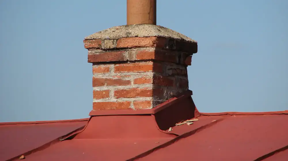Metal flashing sealing the joint where a brick chimney meets a shingle roof