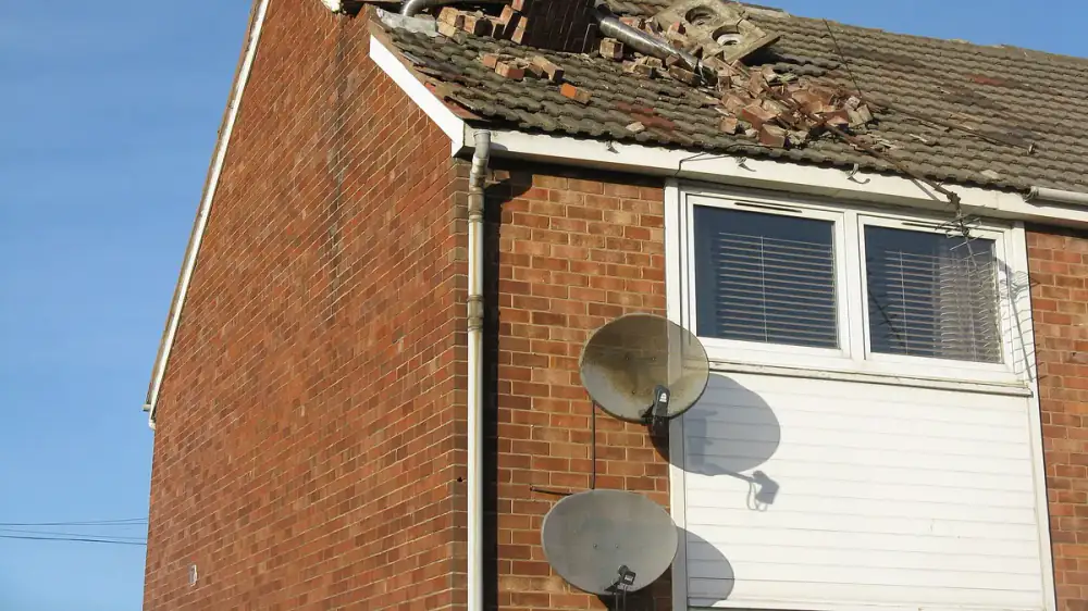 A masonry chimney with a displaced cap and storm debris after high winds