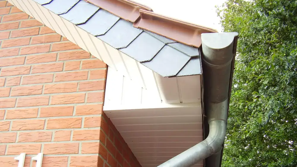 A person fitting a gutter guard panel along a home's roof edge