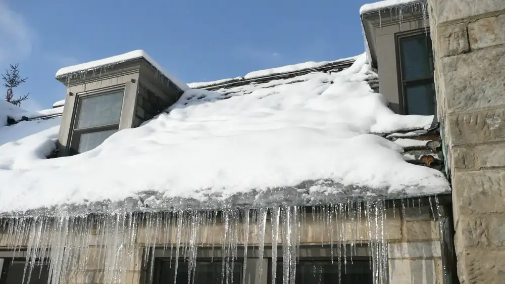 An ice dam and icicles at a roof eave above a snow-covered guarded gutter