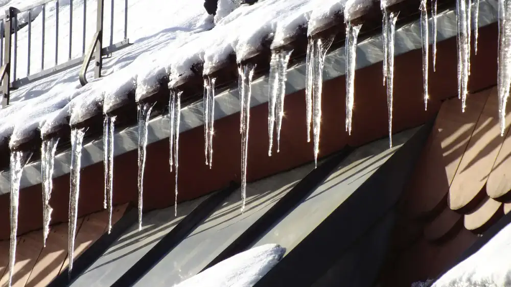 Icicles and snow along a gutter fitted with a guard in winter