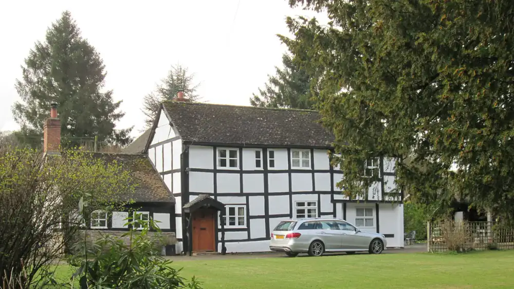 A house partly shaded by mature trees with branches overhanging the roof