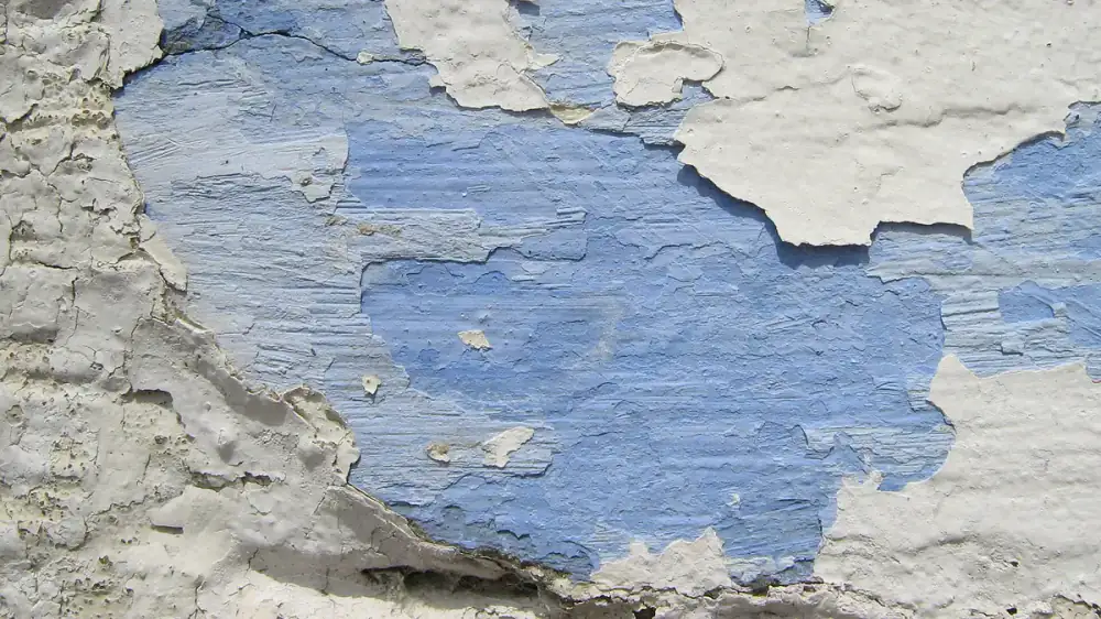 Exterior paint peeling and flaking away from a weathered wood wall