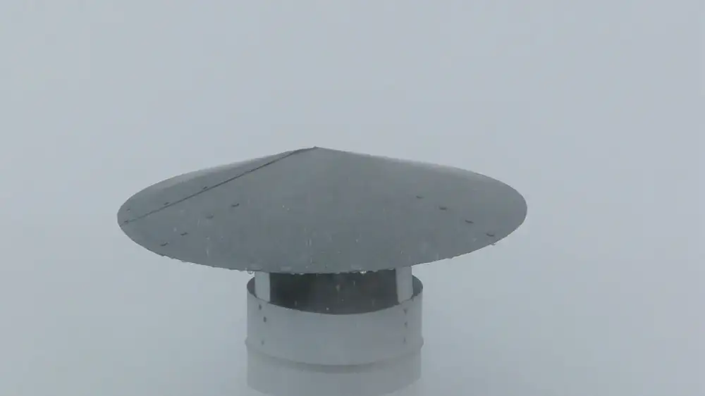 A stainless steel chimney cap with mesh sides on a masonry chimney against a clear sky