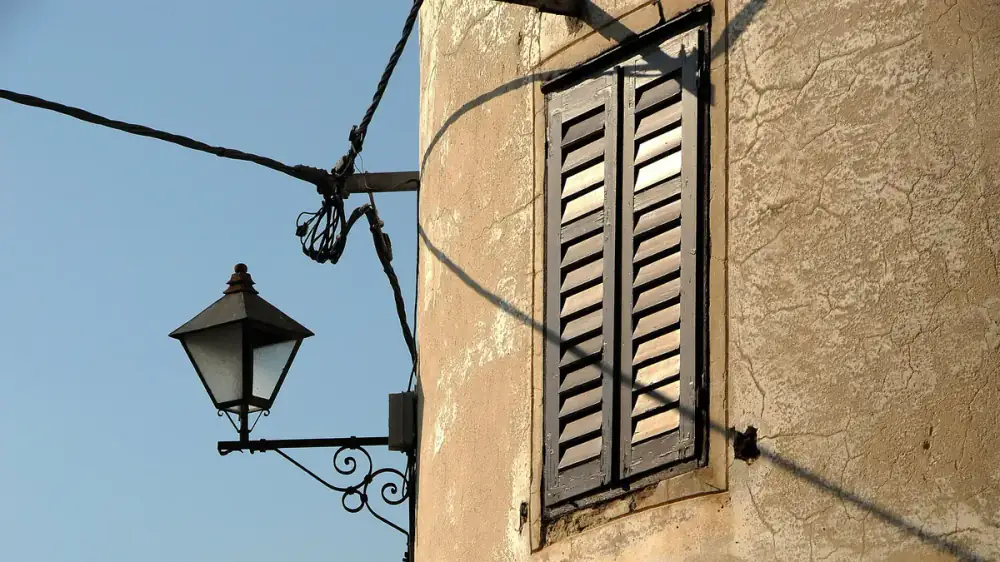 Weathered outdoor wall light fixture with glass panels beside a doorway