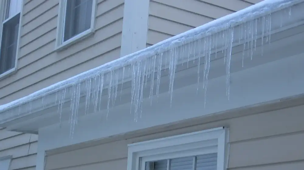 Thick ridge of ice and icicles forming along the edge of a snow-covered roof