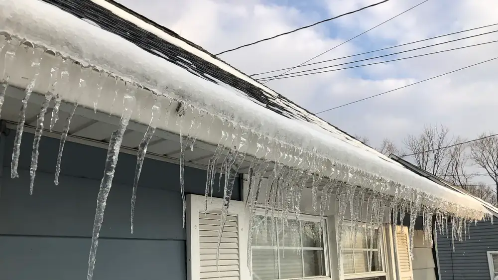 Row of icicles hanging from a home's gutter along a snow-covered roof edge