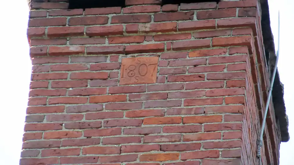 A brick masonry chimney beside a sided prefab chimney chase with a metal chase cover on a residential roof