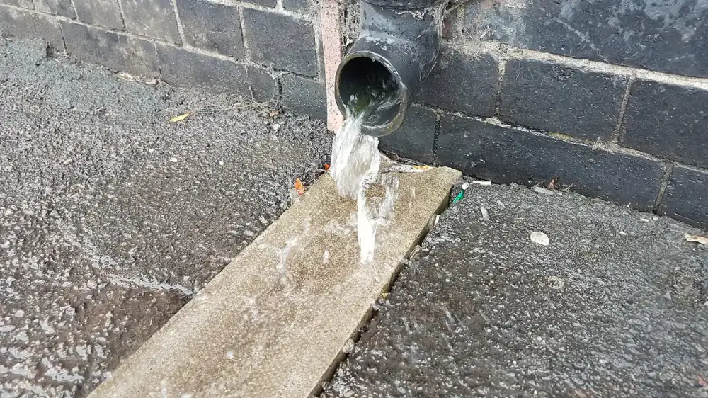 A vertical downspout and elbow at the corner of a house where debris tends to collect